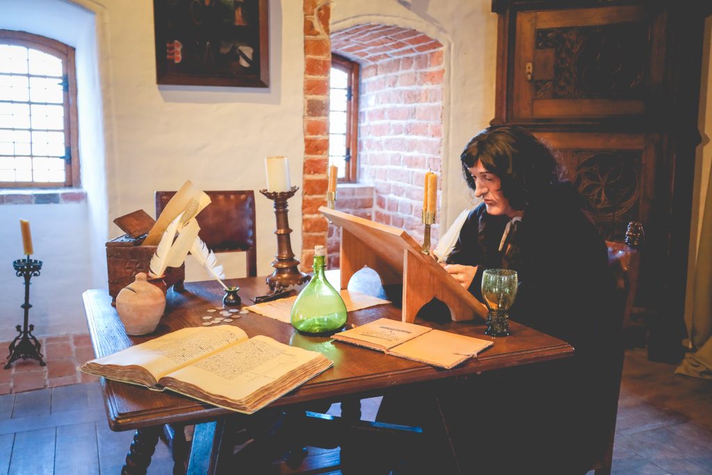 Osoba pisząca w średniowiecznym pomieszczeniu