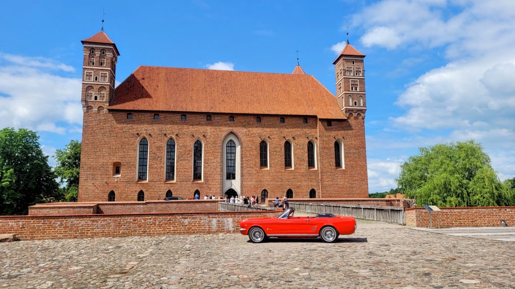 Czerwony samochód kabriolet przed średniowiecznym zamkiem.
