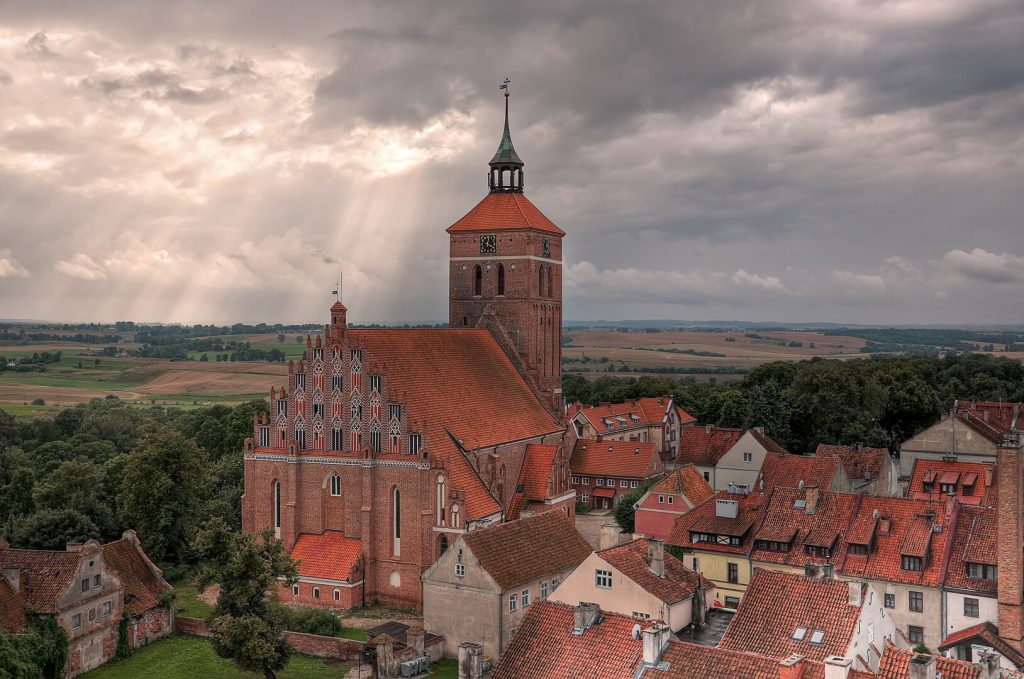 Widok na kościół z czerwonym dachem i zabudowania w tle.