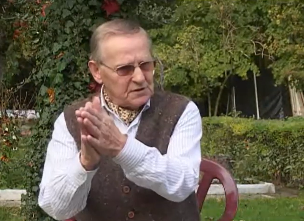 Starszy mężczyzna klaska w dłonie na tle zieleni.