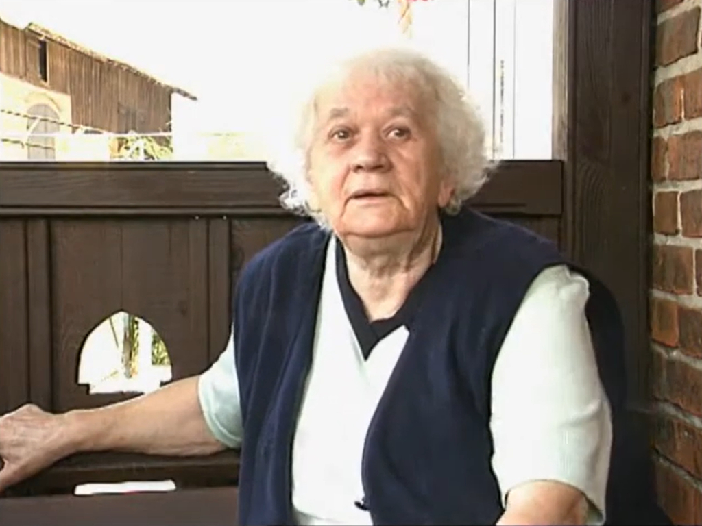 Starsza kobieta siedzi na zewnątrz.