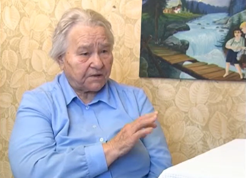 Starsza kobieta w niebieskiej koszuli, gestykulująca podczas rozmowy.