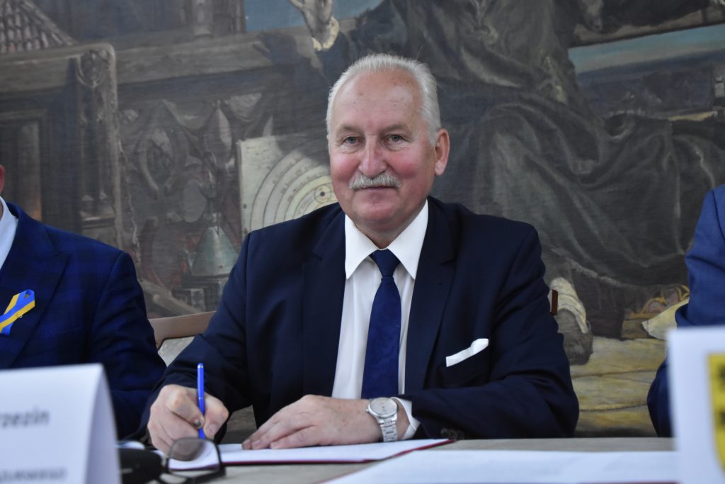 Mężczyzna w garniturze podpisujący dokumenty przy stole.