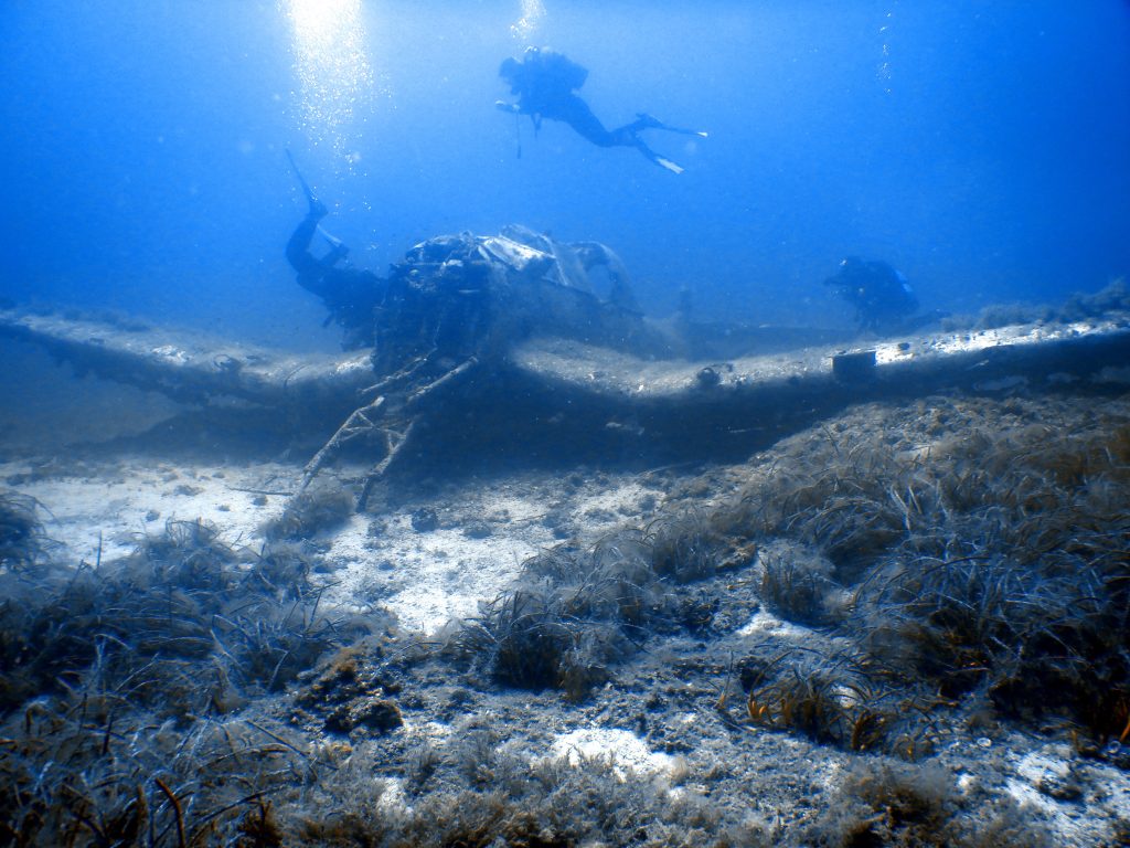 Nurkowie badają wrak samolotu pod wodą.