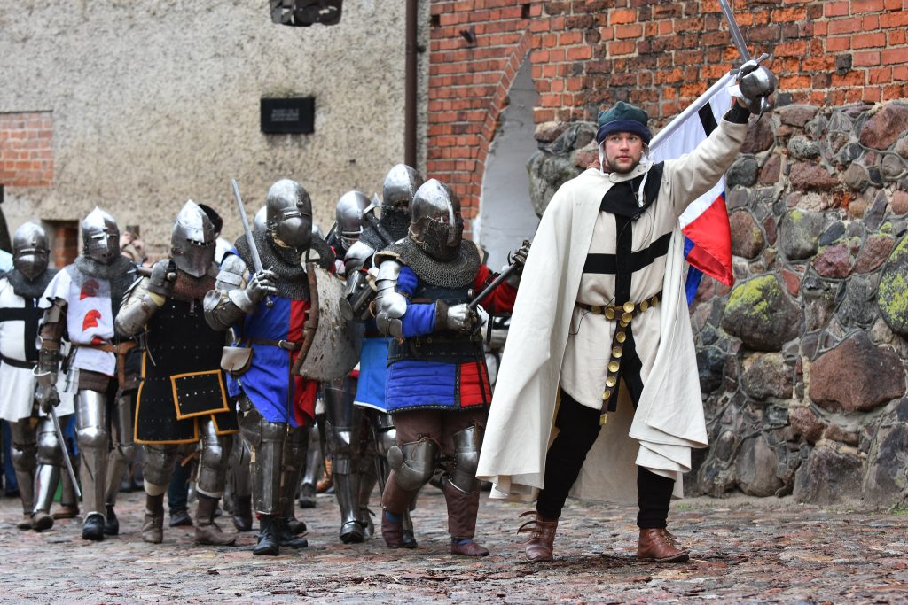 Grupa rycerzy w zbrojach, jedna osoba prowadzi