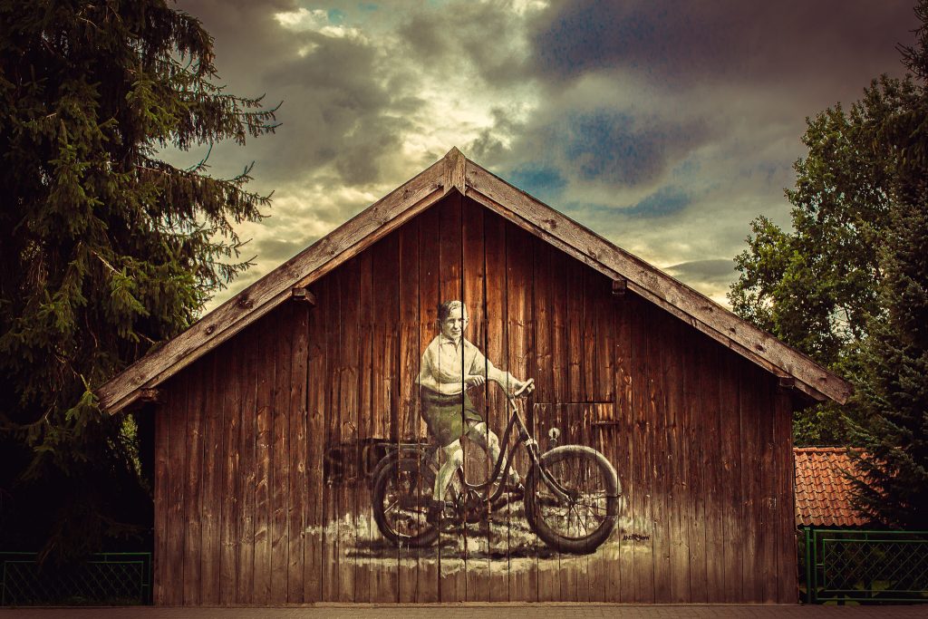 Mural przedstawiający mężczyznę na rowerze na drewnianej ścianie.