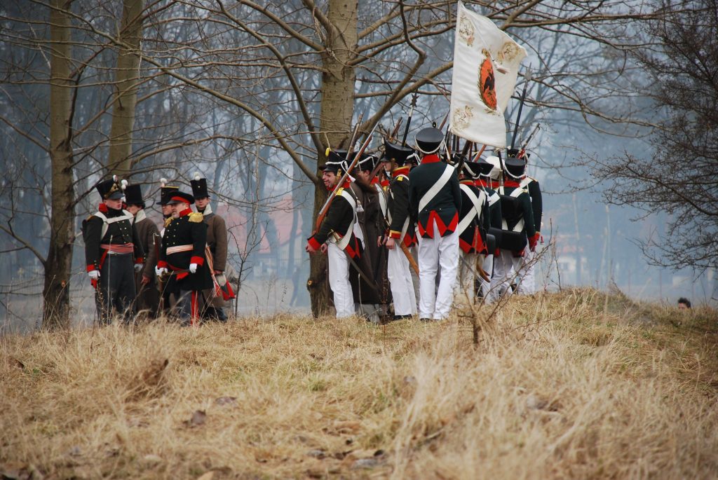 Grupa żołnierzy w historycznych mundurach na tle drzew.