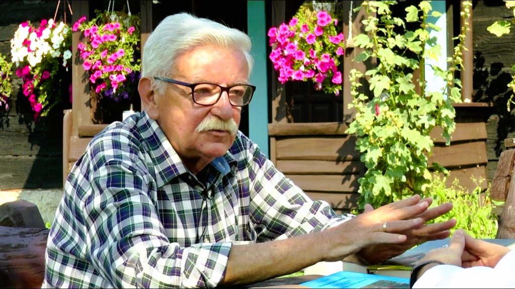 Starszy mężczyzna w kratkę rozmawia na zewnątrz.