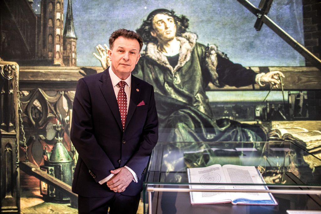 Mężczyzna w garniturze stoi obok książki w muzeum.