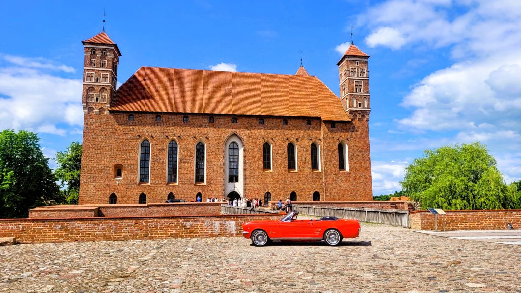 Czerwony samochód sportowy przed zamkiem z cegły.